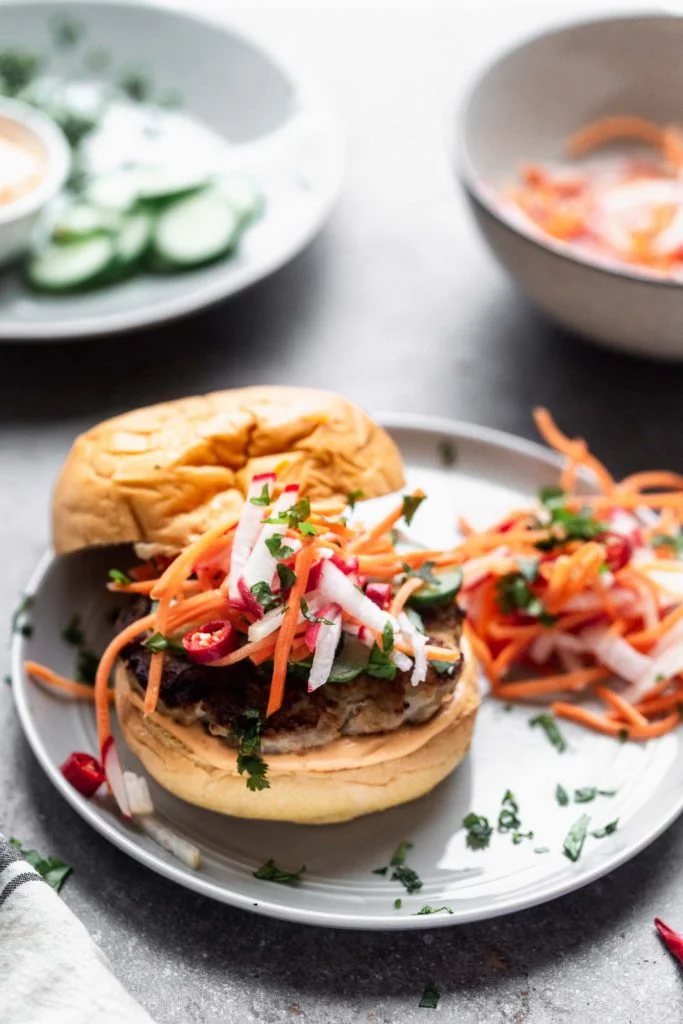 Bánh Mì Chicken Burgers are a burger take on a classic. A ground chicken patty is packed with all the flavors of a classic Bánh Mì sandwich, topped with sweet and spicy pickled veggies, a zippy sriracha mayo, and sandwiched between a toasted brioche bun.