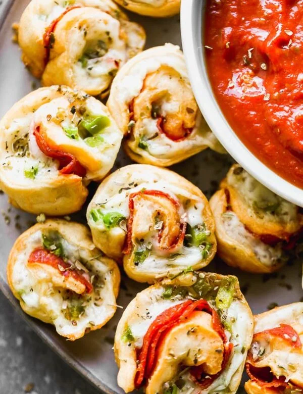 Supreme Pizza Pinwheel Poppers are the perfect Game Day appetizer! Store-bought crescent roll dough is wrapped around shredded mozzarella cheese, spicy pepperoni, and chopped green peppers. They're baked and then served with your favorite pizza sauce (or ranch!) for dipping.