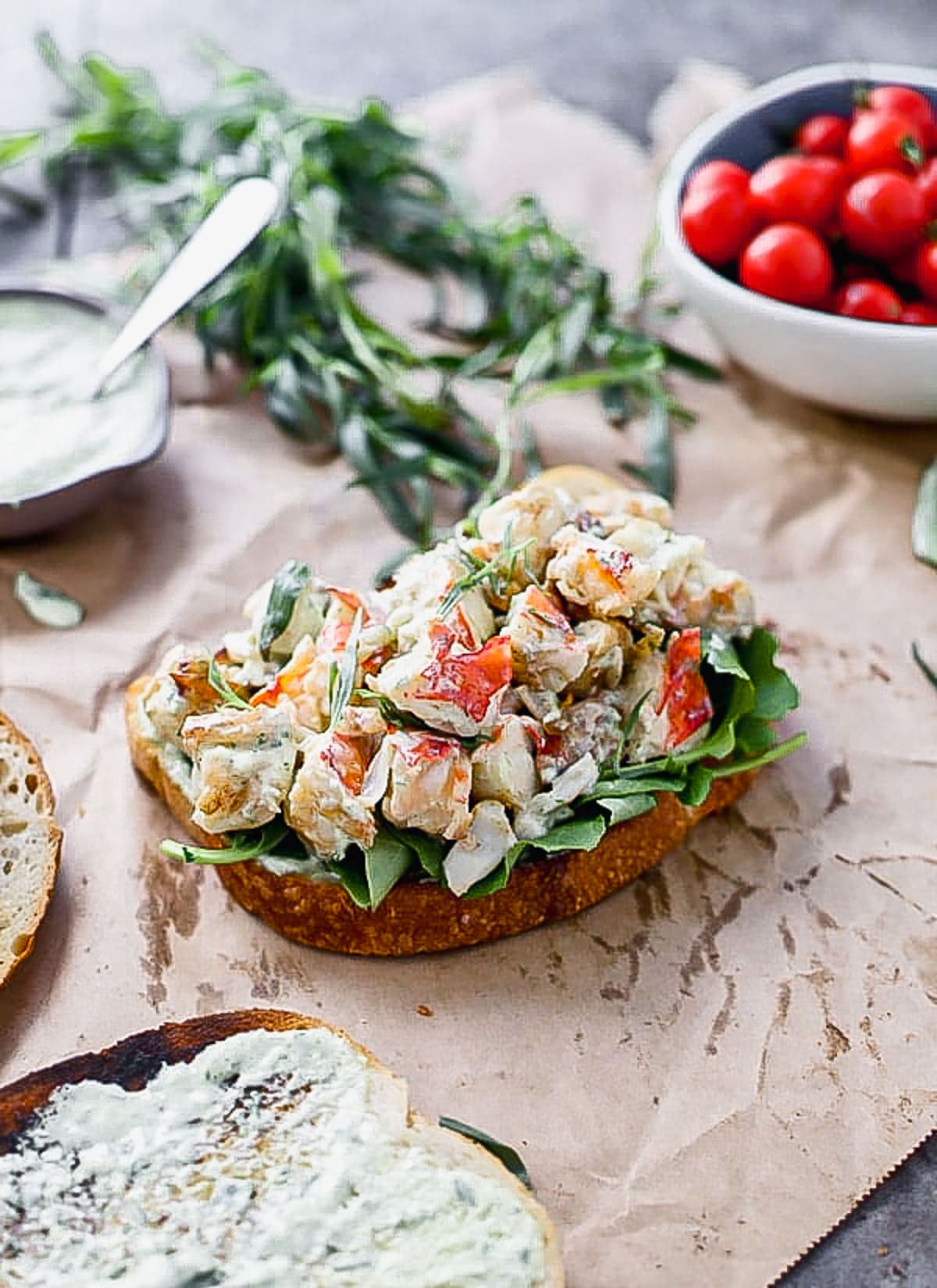 Our Green Goddess Lobster Sandwich Recipe is a dressed-up version of a classic lobster roll. We toss perfectly cooked buttery lobster with a quick green goddess dressing studded with fresh tarragon, basil, and green onion. We pile it high on toasted sourdough bread and top it off with peppery arugula and a squeeze of lemon.
