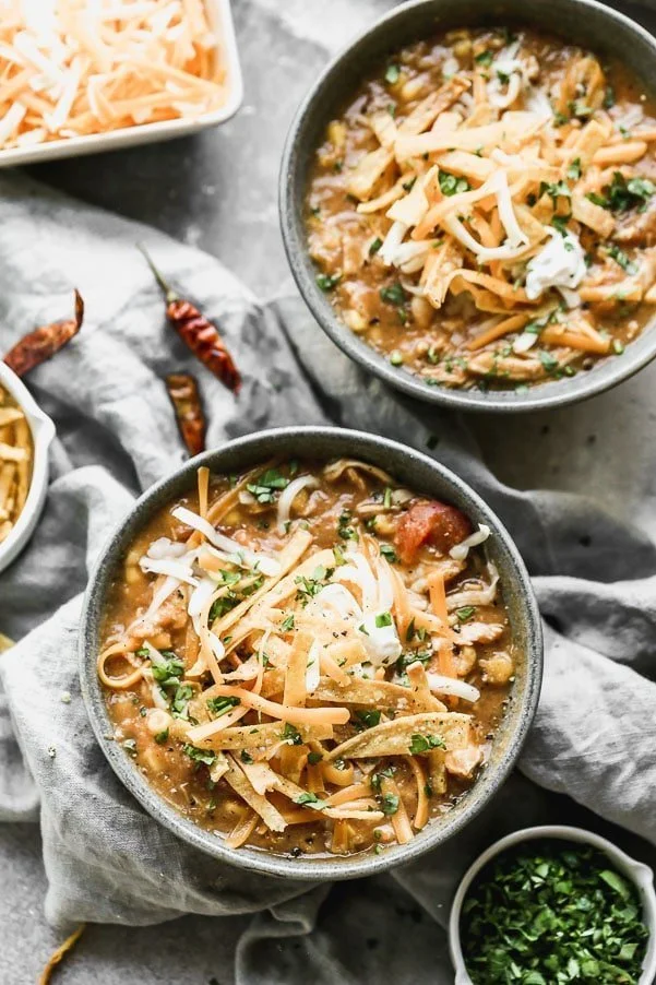 Creamy Chicken Tortilla Soup is spicy, cheesy, creamy, and so delicious! It's packed with dried chiles, canned green chiles and uses corn tortillas instead of cream or cheese for a super creamy texture without adding a ton of fat and calories. Top with homemade tortilla chips, shredded cheese and plenty of sour cream.
