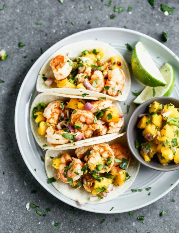 These Easy Chipotle Shrimp Tacos with Mango Salsa are perfect for breezy summer lunches, healthy dinners, or any kind of celebration. Plump shrimp are flavored with chipotle peppers, lime juice, and honey, baked and nestled into corn tortillas (or lettuce wraps!). Each taco is topped off with a quick homemade mango salsa, a little bit of cilantro, and ready to be served!