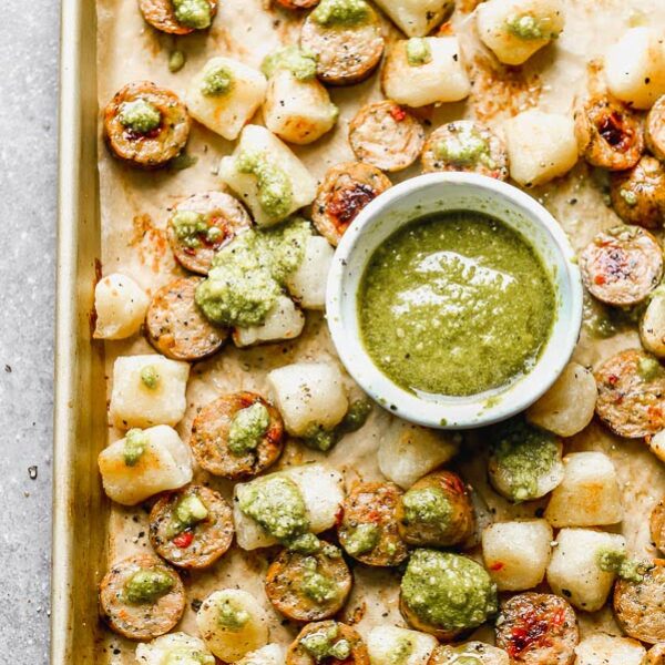 This Baked Cauliflower Gnocchi Recipe is easily the simplest dinner you'll make all year. Cauliflower gnocchi is roasted alongside sun-dried tomato chicken sausage until super crispy and golden brown. When everything comes out of the oven, it's drizzle with a little bit of store-bought pesto and sprinkled with parmesan. It's the perfect healthy, delicious dinner that takes virtually no effort to prepare. 