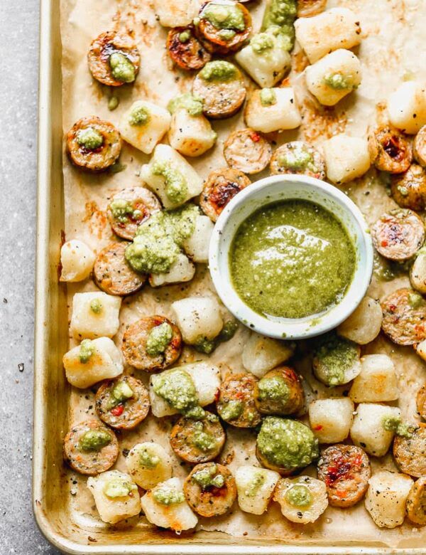 This Baked Cauliflower Gnocchi Recipe is easily the simplest dinner you'll make all year. Cauliflower gnocchi is roasted alongside sun-dried tomato chicken sausage until super crispy and golden brown. When everything comes out of the oven, it's drizzle with a little bit of store-bought pesto and sprinkled with parmesan. It's the perfect healthy, delicious dinner that takes virtually no effort to prepare. 
