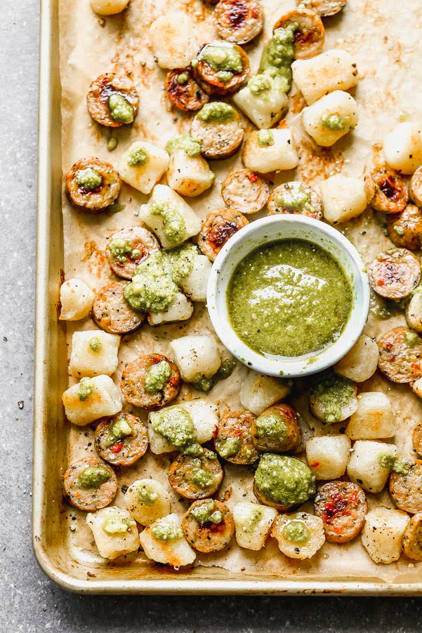 This Baked Cauliflower Gnocchi Recipe is easily the simplest dinner you'll make all year. Cauliflower gnocchi is roasted alongside sun-dried tomato chicken sausage until super crispy and golden brown. When everything comes out of the oven, it's drizzle with a little bit of store-bought pesto and sprinkled with parmesan. It's the perfect healthy, delicious dinner that takes virtually no effort to prepare.&nbsp;