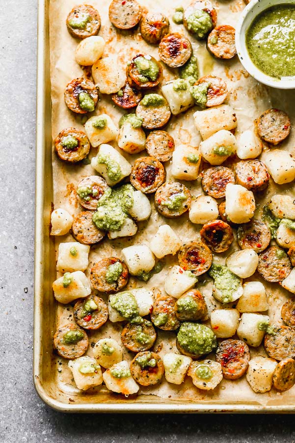 This Baked Cauliflower Gnocchi Recipe is easily the easiest dinner you'll make all year. Cauliflower gnocchi is roasted alongside sun-dried tomato chicken sausage until super crispy and golden brown. When everything comes out of the oven, it's drizzle with a little bit of store-bought pesto and sprinkled with parmesan. It's the perfect healthy, delicious dinner that takes virtually no effort to prepare.&nbsp;