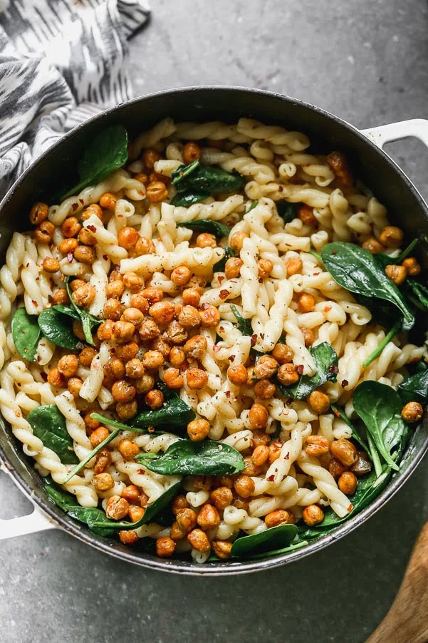 Pasta e Ceci Alla Romana (Pasta with Chickpeas) is a light, hearty, and healthy pasta dish. Aldente gemelli pasta is tossed with garlic, lemon, plenty of crushed red pepper flakes and just enough starchy pasta water to make a light sauce. It's also packed with crispy chickpeas, sweet roasted garlic and tender spinach leaves.&nbsp;