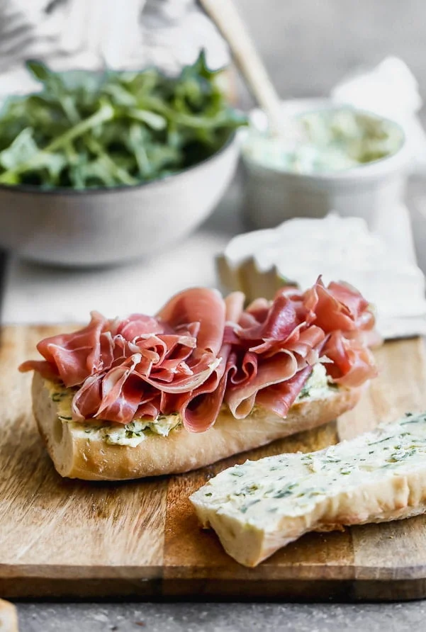 Layer prosciutto on top of a French baguette spread with herbed butter