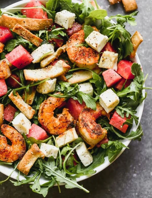Blackened Shrimp and Halloumi Salad - have you seen a prettier combination? We take take peppery arugula leaves and toss them in a simple vinaigrette and then layer them with sweet watermelon, salty halloumi cheese, toasted pita croutons, and spicy blackened shrimp. It's hearty, healthy, and SO delicious. 