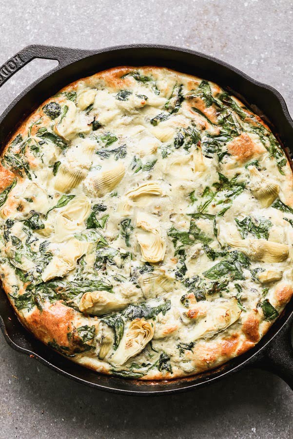 Impress family and friends with this Cheesy Artichoke and Spinach Frittata for your next brunch! This easy egg dish comes together in no time with virtually no effort. It's packed with hearty spinach, artichoke hearts, and nutty parmesan cheese. Once the fluffy frittata is just shy of being done, we dollop fresh pesto on top and sprinkle with shredded Monterrey jack cheese. Healthy, but totally satisfying!&nbsp;