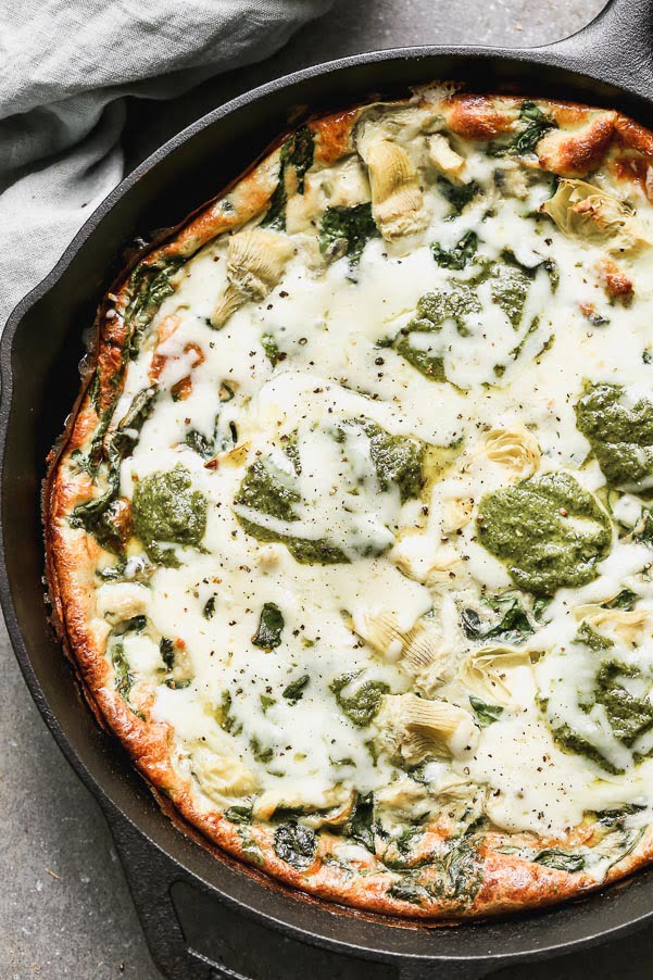 Impress family and friends with this Cheesy Artichoke and Spinach Frittata for your next brunch! This easy egg dish comes together in no time with virtually no effort. It's packed with hearty spinach, artichoke hearts, and nutty parmesan cheese. Once the fluffy frittata is just shy of being done, we dollop fresh pesto on top and sprinkle with shredded Monterrey jack cheese. Healthy, but totally satisfying! 