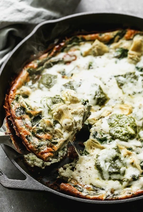 Impress family and friends with this Cheesy Artichoke and Spinach Frittata for your next brunch! This easy egg dish comes together in no time with virtually no effort. It's packed with hearty spinach, artichoke hearts, and nutty parmesan cheese. Once the fluffy frittata is just shy of being done, we dollop fresh pesto on top and sprinkle with shredded Monterrey jack cheese. Healthy, but totally satisfying!&nbsp;