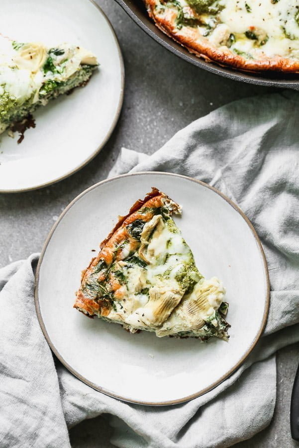 Impress family and friends with this Cheesy Artichoke and Spinach Frittata for your next brunch! This easy egg dish comes together in no time with virtually no effort. It's packed with hearty spinach, artichoke hearts, and nutty parmesan cheese. Once the fluffy frittata is just shy of being done, we dollop fresh pesto on top and sprinkle with shredded Monterrey jack cheese. Healthy, but totally satisfying! 