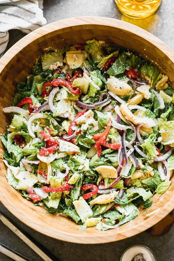 Italian Artichoke Salad is our go-to salad for cozy winter dinners, alfresco summer barbecues and everything in between. We marinate artichoke hearts and red onions in a zippy red wine and parmesan vinaigrette, toss everything with crisp romaine lettuce and sliced roasted red peppers. Easy to make ahead of time, perfect to feed a large family, and delicious.&nbsp;