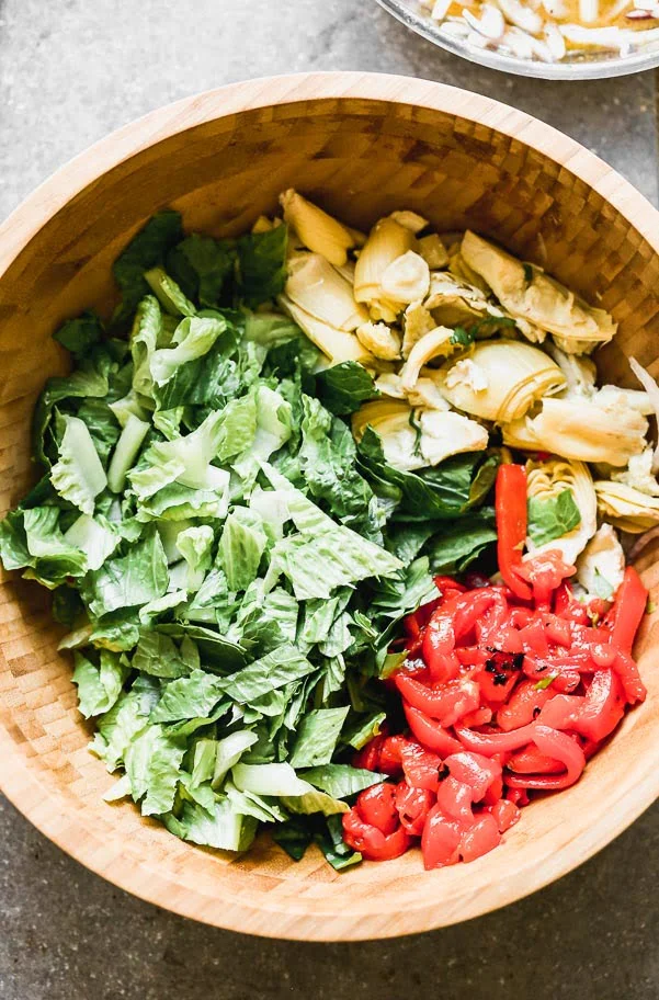 Romaine lettuce, artichoke hearts, roasted red peppers in a large salad bowl