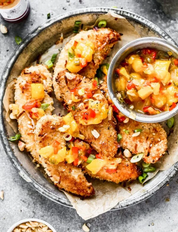 Let's all satisfy the kid in us with these ultra crispy, completely irresistible Baked Coconut Chicken Tenders. We coat tender chicken in a light coconut and panko breading, bake them on a screaming hot baking sheet and then serve them with a quick warm mango salsa and a hot honey drizzle. 