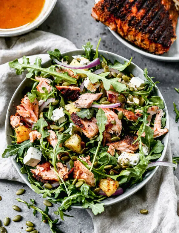 We toss peppery arugula with salty feta, crunchy pepita seeds, red onion and an easy honey vinaigrette. We add in grilled blackened salmon and pineapple to make this easy salad hearty and perfect for lunch or dinner.