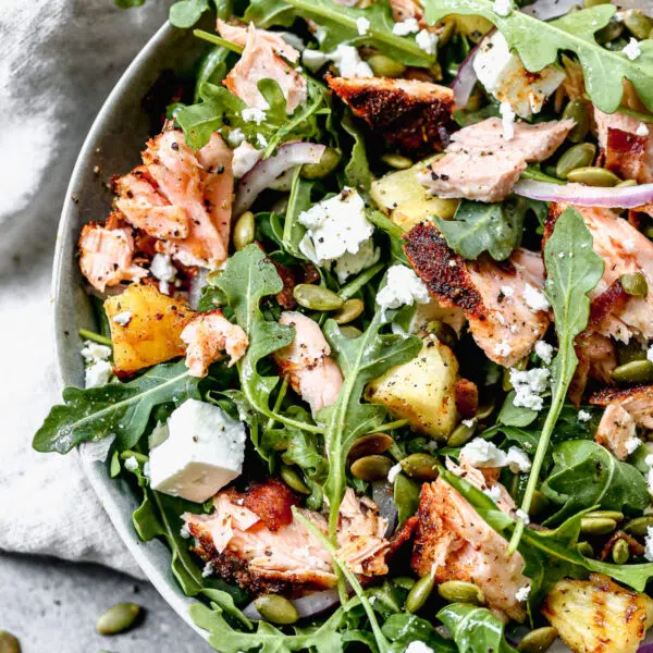 We toss peppery arugula with salty feta, crunchy pepita seeds, red onion and an easy honey vinaigrette. We add in grilled blackened salmon and pineapple to make this easy salad hearty and perfect for lunch or dinner.