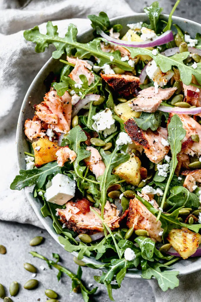 We toss peppery arugula with salty feta, crunchy pepita seeds, red onion and an easy honey vinaigrette. We add in grilled blackened salmon and pineapple to make this easy salad hearty and perfect for lunch or dinner.
