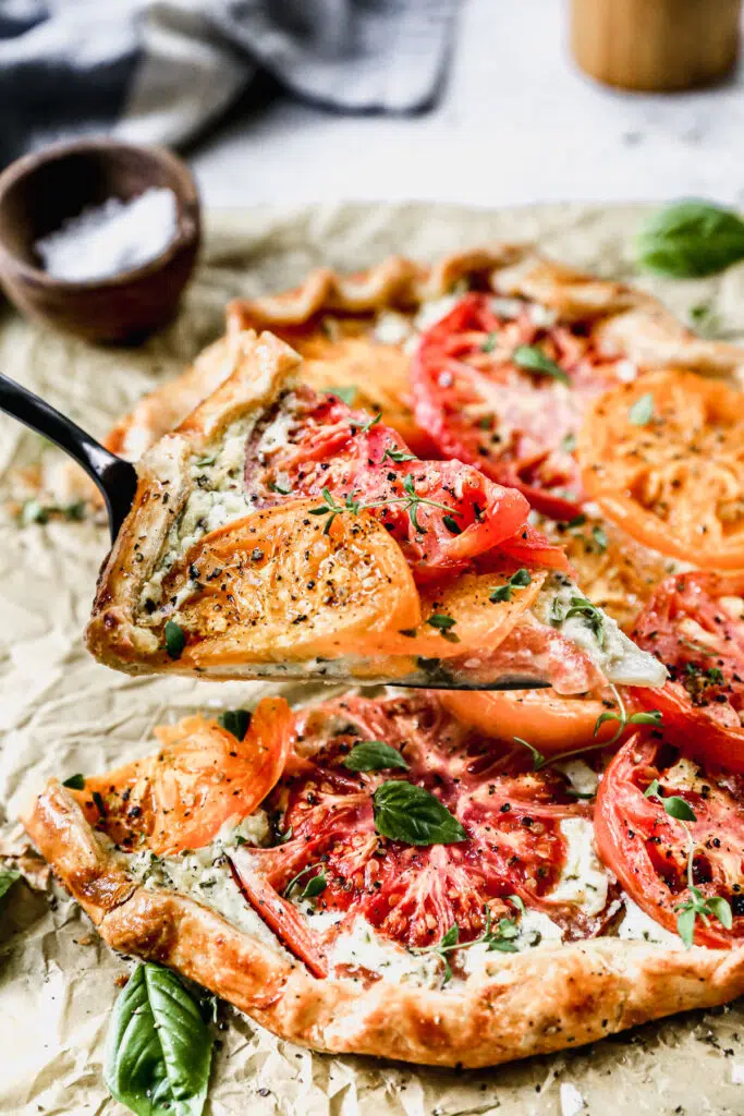 With a hidden layer of basil and gruyere-laced ricotta smothered on top of a store-bought pie crust and topped with juicy jewel-toned tomatoes, our Tomato Galette Recipe is just what you need to round out your summer.