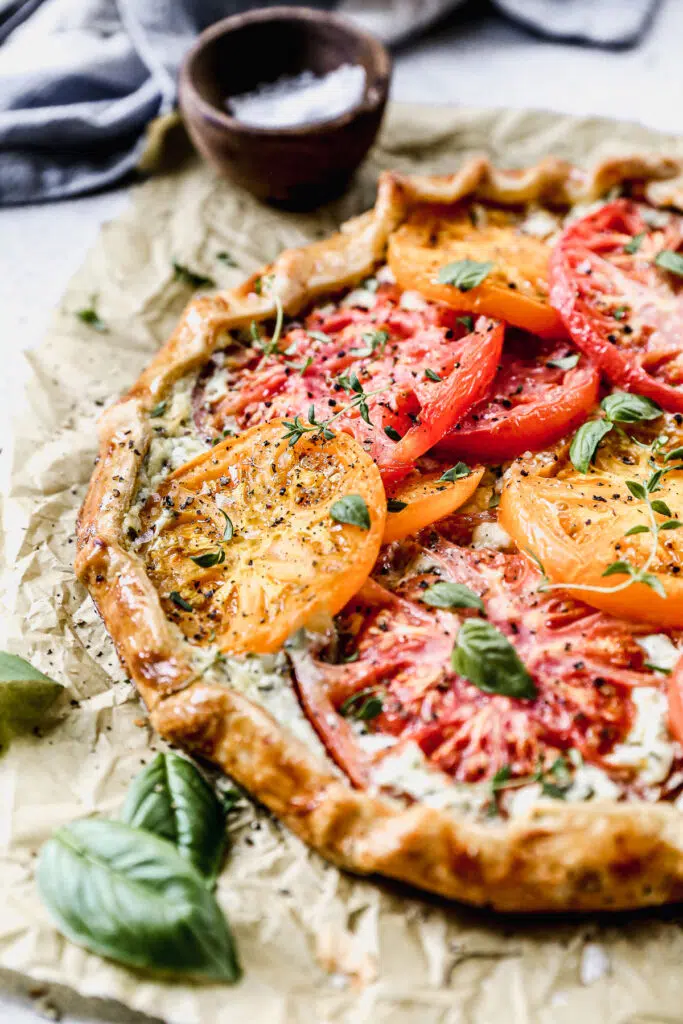 With a hidden layer of basil and gruyere-laced ricotta smothered on top of a store-bought pie crust and topped with juicy jewel-toned tomatoes, our Tomato Galette Recipe is just what you need to round out your summer.