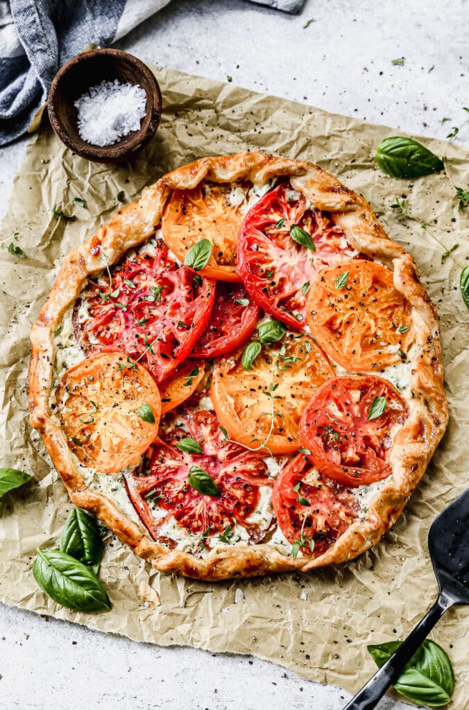  With a hidden layer of basil and gruyere-laced ricotta smothered on top of a store-bought pie crust and topped with juicy jewel-toned tomatoes, our Tomato Galette Recipe is just what you need to round out your summer. 