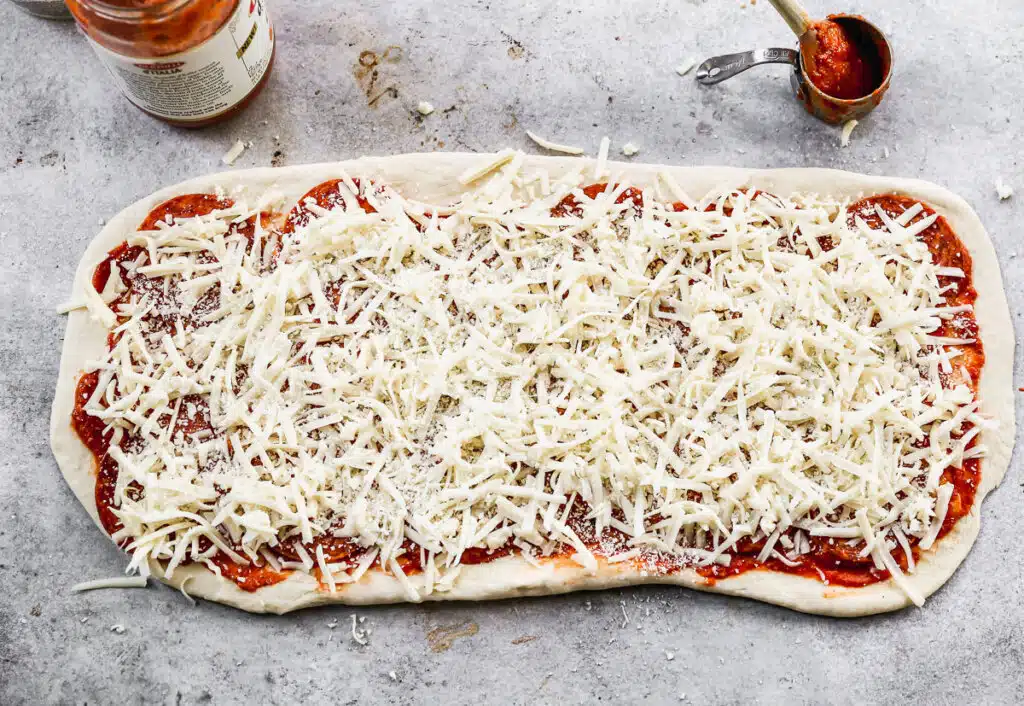 Cheese sprinkled on pizza dough, sauce and pepperoni