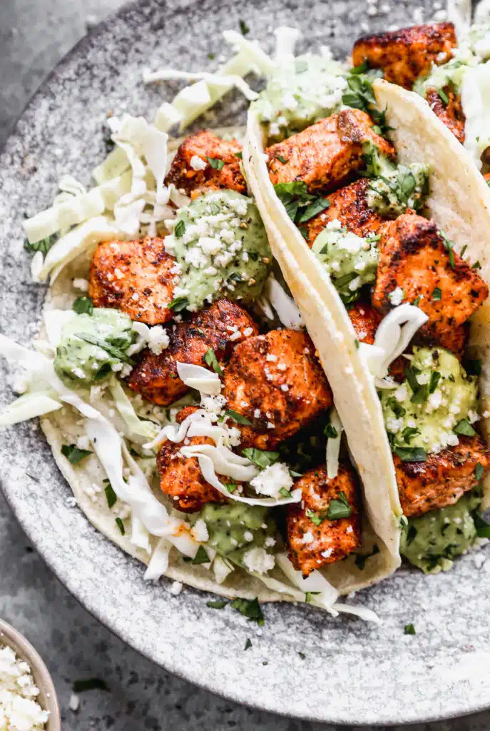 Stuffed with buttery blackened salmon bites and shredded cabbage then drizzled with a luscious Jalapeño cilantro Crema and crumbled Cotija cheese, our salmon tacos are sure to hit the seafood spot.