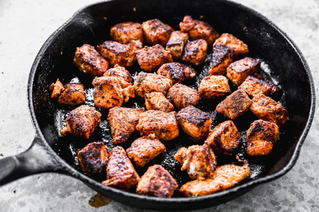 Blackened salmon bites cooking in cast iron skillet