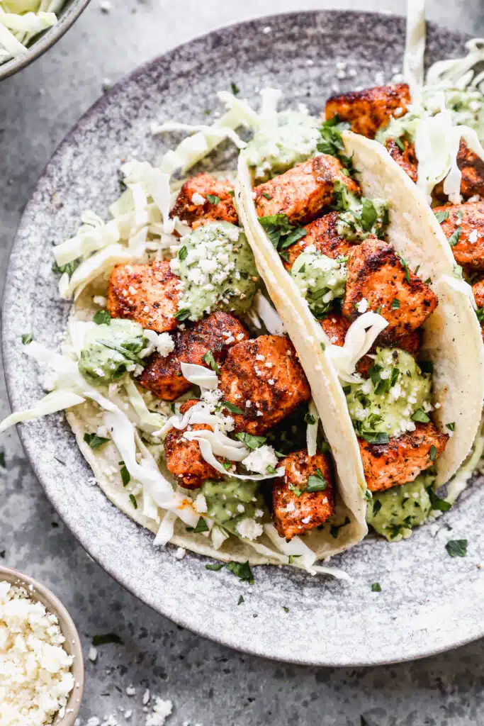 Stuffed with buttery blackened salmon bites and shredded cabbage then drizzled with a luscious Jalapeño cilantro Crema and crumbled Cotija cheese, our salmon tacos are sure to hit the seafood spot.