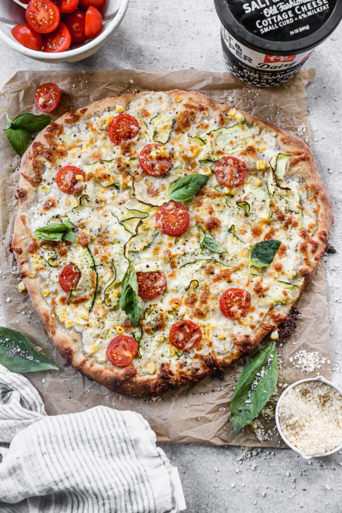Cottage Cheese Pizza is the summer pie you never knew you needed. With a creamy, tangy cottage cheese and sharp provolone base and a delicate shaved zucchini, sweet corn and cherry tomato topping, this veggie forward pizza is truly a winner.