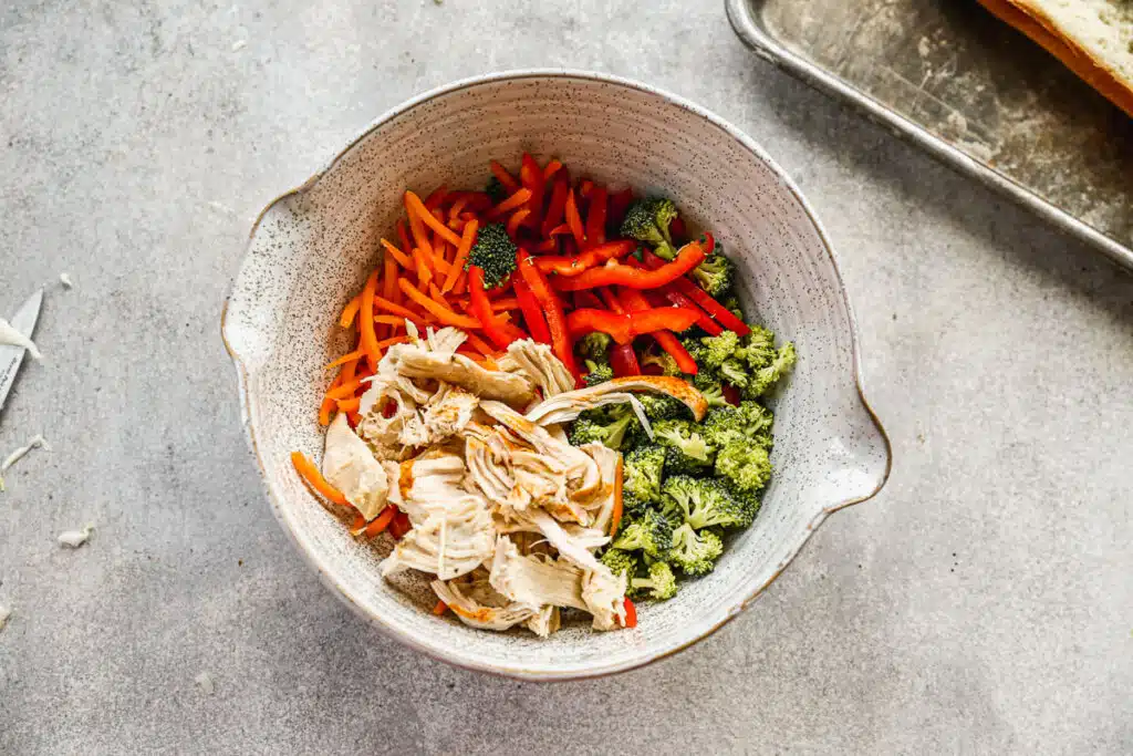 Broccoli, chicken, carrots and red pepper in a mixing bowl