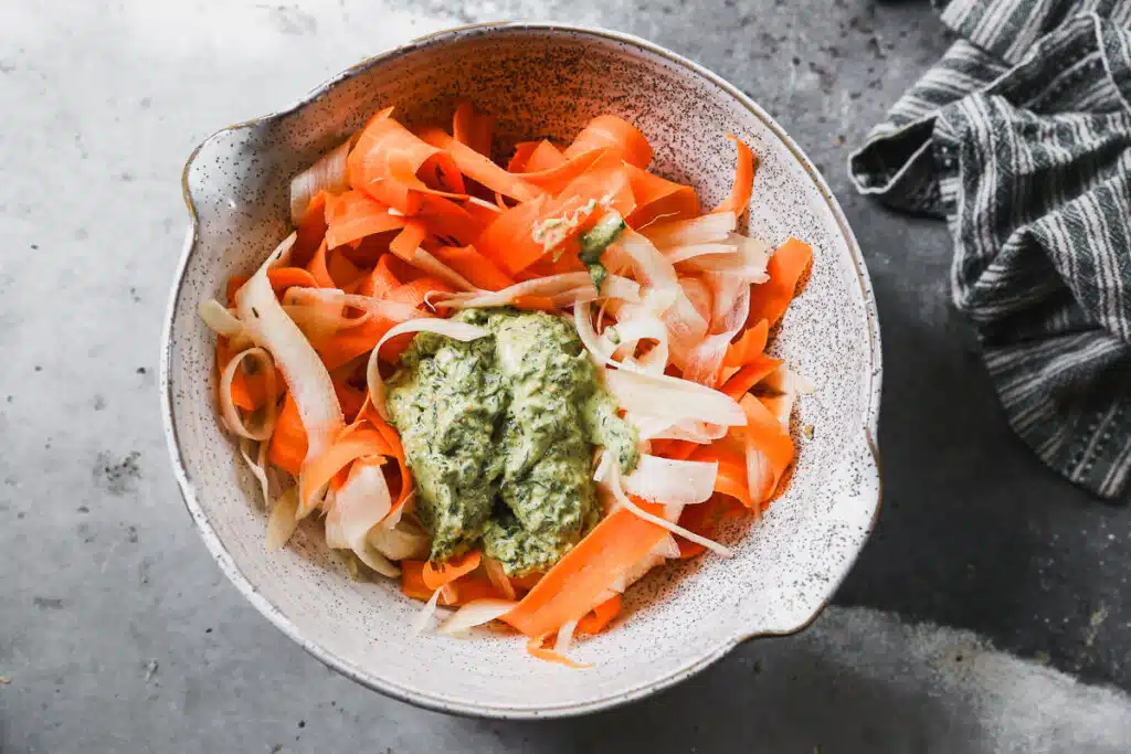 Shaved carrots with pesto in a mixing bowl