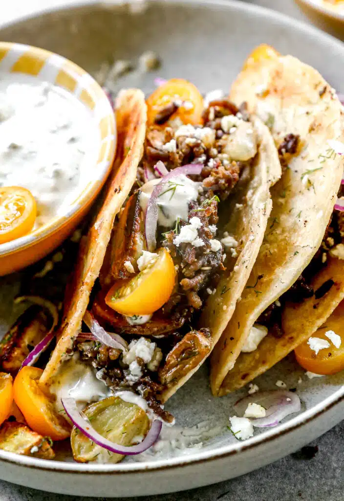 Our lamb tacos are stuffed with gyro-flavored lamb, tangy feta cheese and crisped to perfection in a hot cast-iron skillet. After the tortilla becomes ultra crispy and the feta melts into a tangy oblivion, we open them up and stuff each taco with store-bought tzatziki (another shortcut), juicy cherry tomatoes, paper-thin red onions, and plenty of fresh dill.
